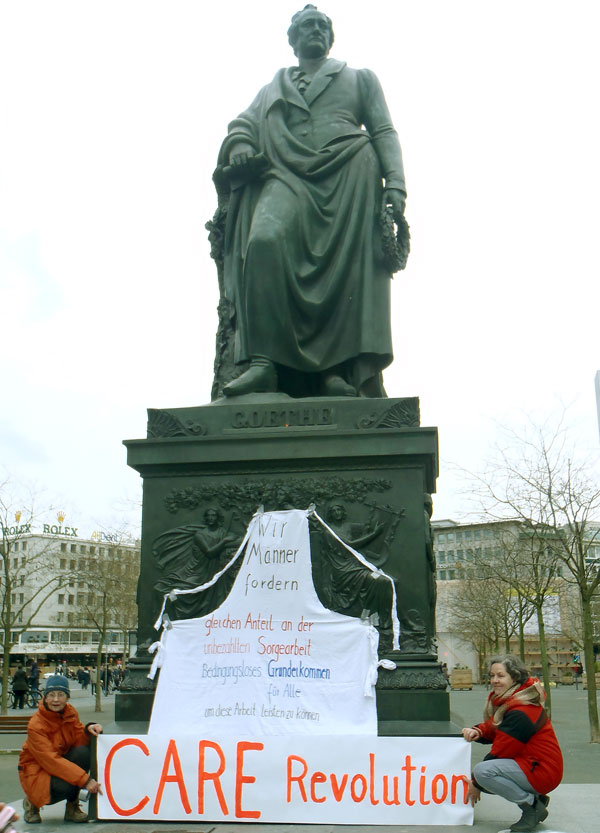 Goethestatue mit Schuerze auf der die Forerung steht: Gleicher Anteil an Sorgearbeit fuer Maenner und Frauen, BGE fuer alle.