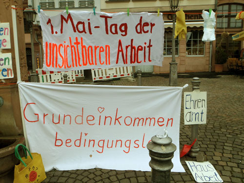 1.Mai Kundgebung. Banner mit Aufschrift 1. Mai Tag der unsichtbaren Arbeit und Bedingungsloses Grundeinkommen