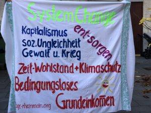 Banner mit der Aufschrift: System Change. Kapitalismus, soz. Ungleichheit, Gewalt und krieg entsorgen., Zeit-Wohlstand + Klimaschutz, Bedingungsloses Grundeinkommen