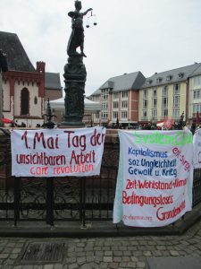Banner am Justiziabrunnen in Frankfurt mit der Aufschrift: 1. Mai Tag der unsichtbaren Arbeit, und yum Bedingungslosen Grundeinkommen